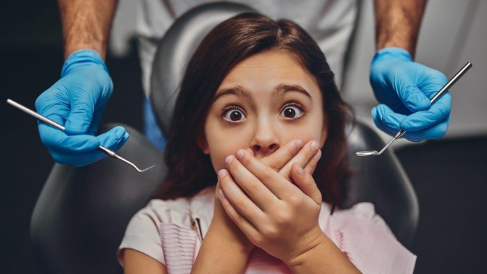 girl afraid of the dentist and clasping her hands over mouth