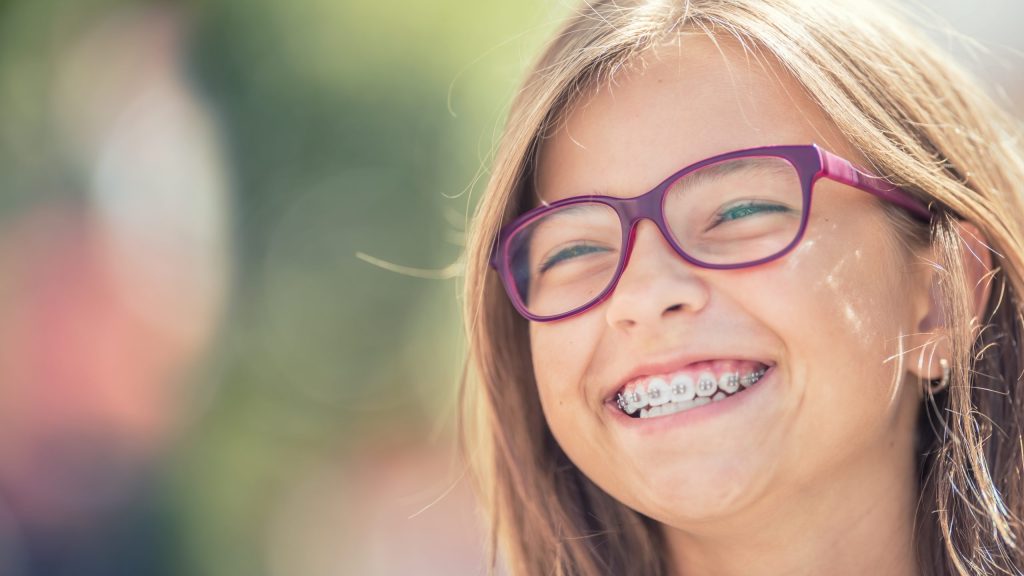 Young girl with purple glasses and braces smiling Grandville MI pediatric dentists